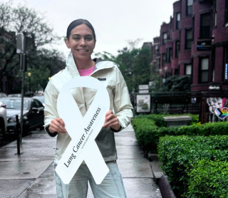Ashley, standing outside in SF, holding a white lung cancer awareness ribbon