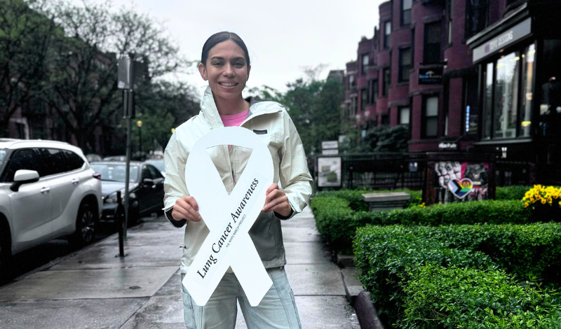 Ashley, standing outside in SF, holding a white lung cancer awareness ribbon