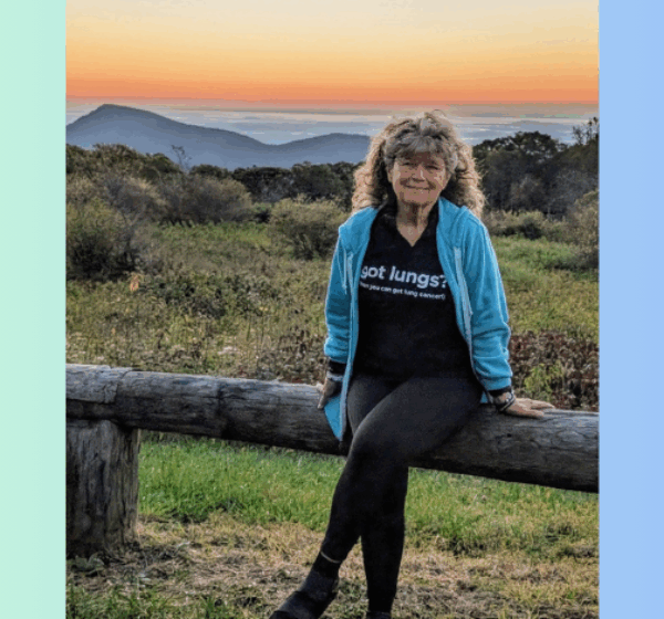 Donnita Butler sitting on a log railing with a beautiful sunset behind her.