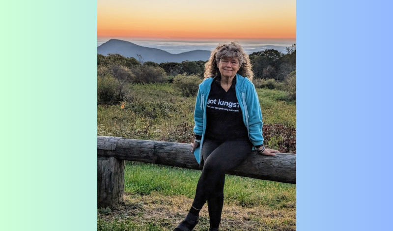 Donnita Butler sitting on a log railing with a beautiful sunset behind her.