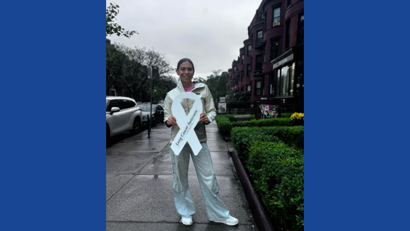 A woman holds a white ribbon on a rainy sidewalk.