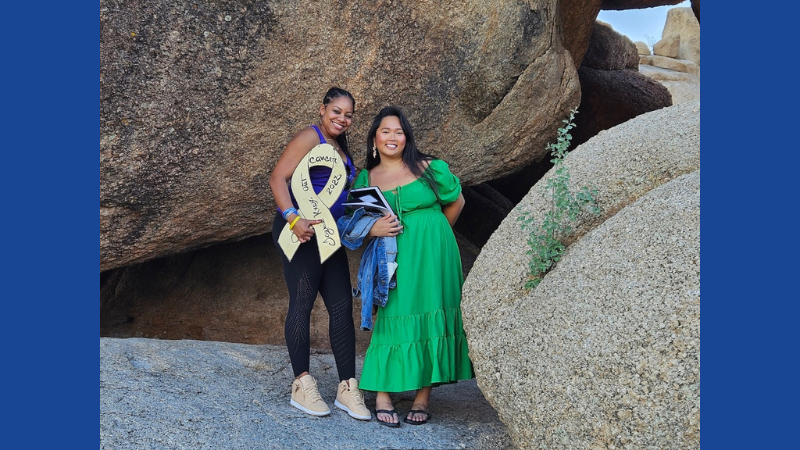 Two women hold a white ribbon in front of large boulders.