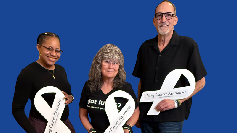 Three people, two women and one man, show off their white ribbon cardboard cutouts.