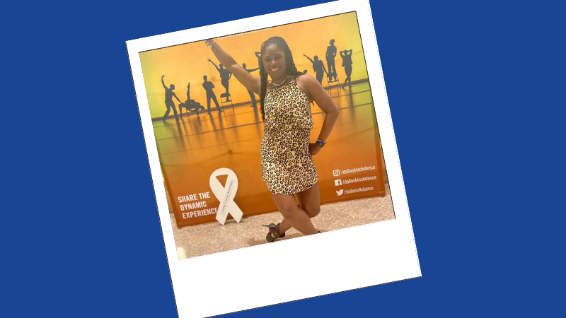 A woman poses in front of a dance poster with her white ribbon cardboard cutout.