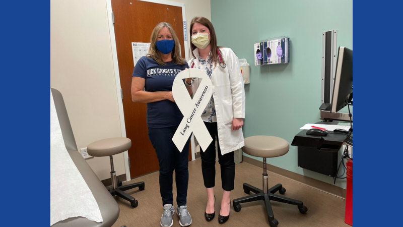 A woman holds a white ribbon cutout next to a doctor.